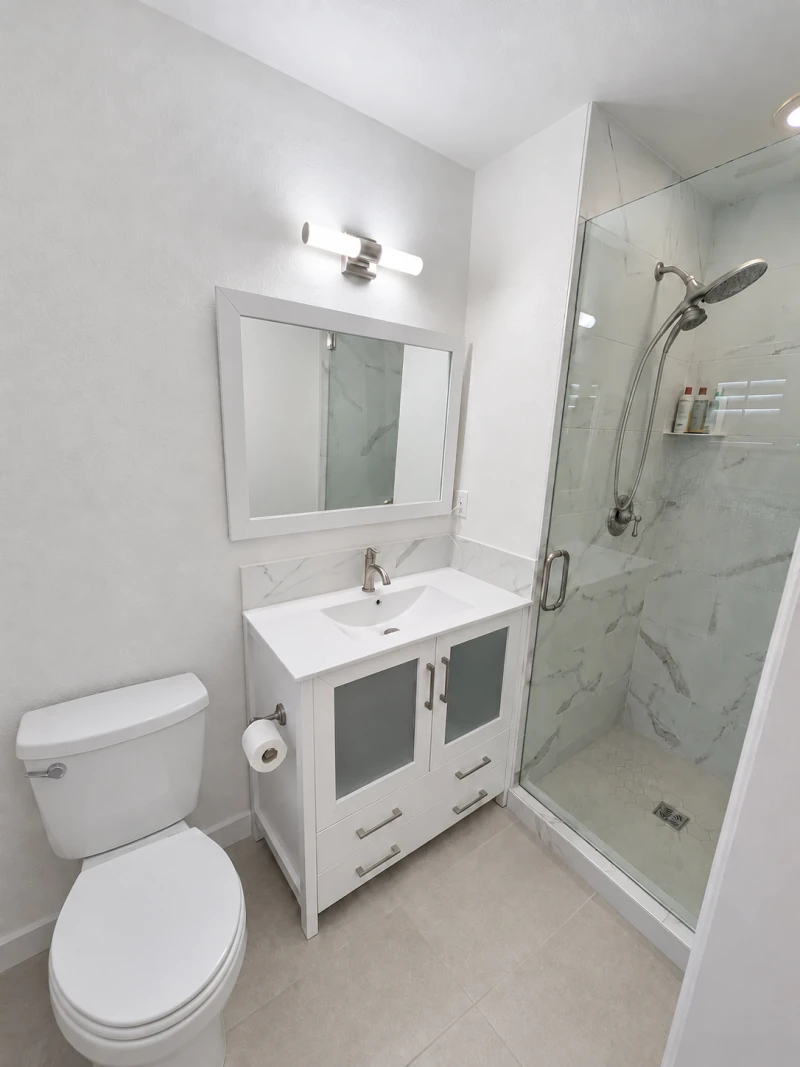 Completed Olive Street bathroom with a clear white vanity, closed toilet lid and gray-veined marble shower
