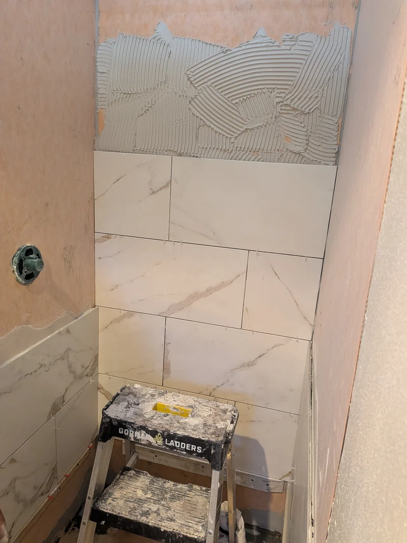 Olive Street shower tile being installed, with unfinished wall areas and a step stool